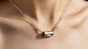 A small elegant pendant device worn as a necklace with a subtle LED indicator and minimalist jewelry aesthetic in a lifestyle fashion photography setting