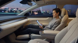Person relaxing in the backseat of an autonomous vehicle reading on a tablet with no steering wheel visible